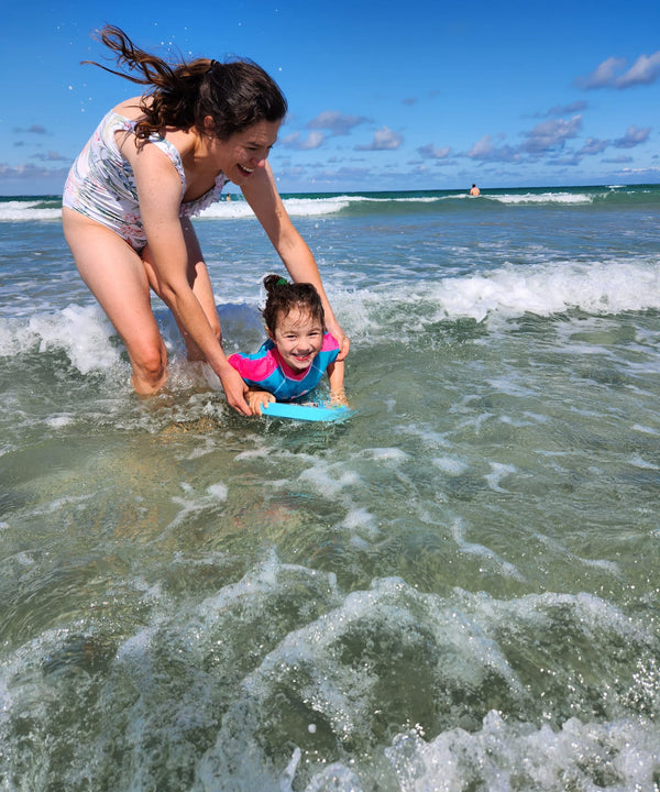 Woman and child standing together in the sea, enjoying the calm waters and warm sunlight, creating a peaceful and serene moment by the shore.